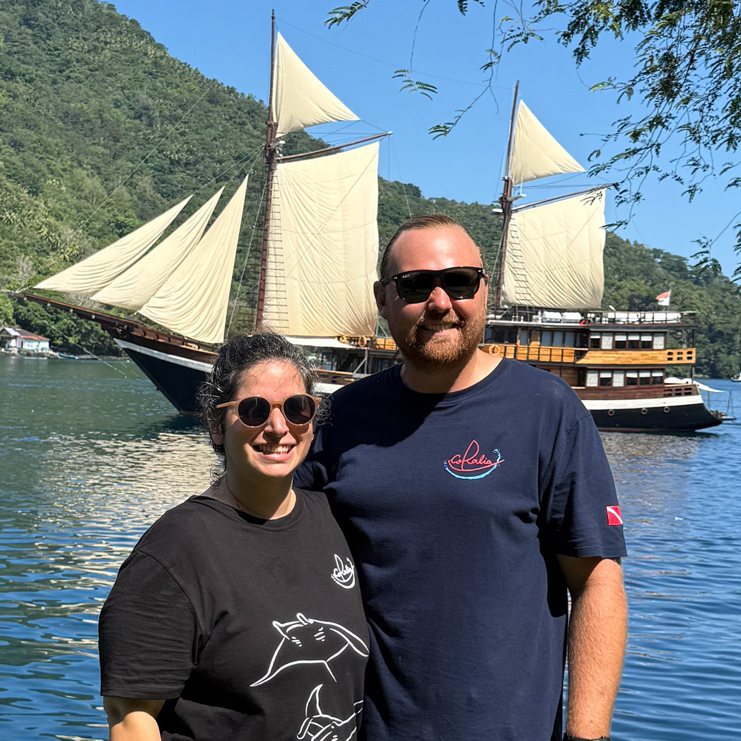 Cruise Directors Jacob and Amanda in the Banda Islands with Coralia Liveaboard with the sails up in the background